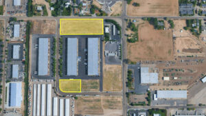 Aerial view of an industrial area with two vacant lots outlined in yellow along a road (one large rectangle up top, one small curved rectangle bottom left).