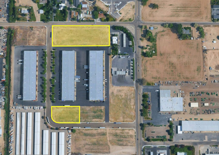 Aerial view of an industrial area with two vacant lots outlined in yellow along a road (one large rectangle up top, one small curved rectangle bottom left).