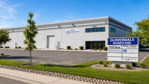 Industrial warehouse building with a large 'Cloverdale Business Park' sign in front; blue sky, parking lot, and landscaping nearby.
