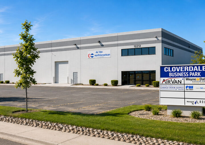 Industrial warehouse building with a large 'Cloverdale Business Park' sign in front; blue sky, parking lot, and landscaping nearby.
