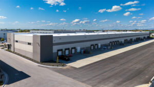 Modern warehouse with multiple loading docks along a long building under a bright blue sky with scattered clouds