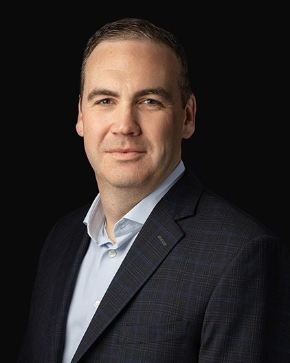 Professional headshot of a man in a dark plaid blazer and light blue shirt, set against a black background, looking confident at the camera.