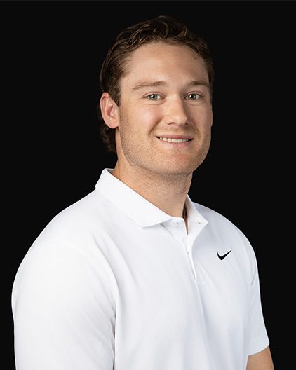 Portrait of a smiling man in a white polo shirt against a black background, facing slightly right.