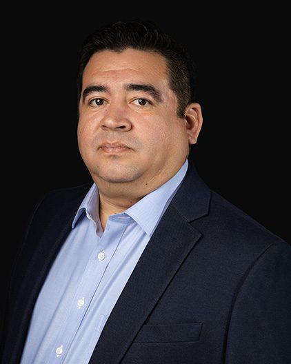 Professional head-and-shoulders portrait of a man in a navy blazer and light blue shirt against a black background.