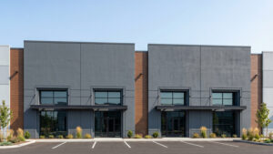 Modern, gray commercial building with two entrance doors, large windows, and brown vertical accent panels, front landscaping.