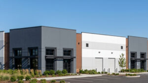 Modern commercial building exterior with gray and white panels, brown accents, and landscaped parking lot under a clear blue sky